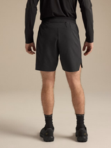 Rear view of a person wearing black athletic shorts, a black long-sleeve top, black socks, and black shoes against a plain beige studio background. - Arc'teryx Norvan Liner Shorts 7" (Men's) - Black