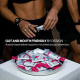 A plate of ALJAB branded pectin packets sits on a white table, with a cropped view of two people in black athletic wear reaching toward the packets. White text reads 'GUT AND MOUTH FRIENDLY BY DESIGN' and 'A pectin base delivers superior mouthfeel and gut protection. - Pillar Performance Energy Gel 30
