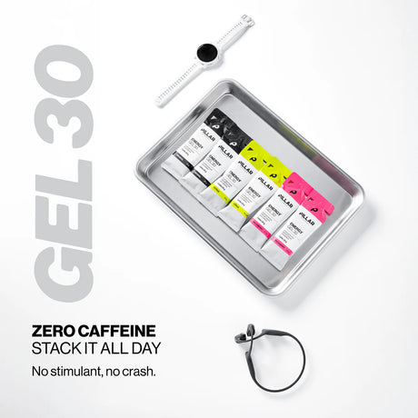 A promotional flat lay on a white background showing a silver tray with four small gel packets in black, white, yellow, and pink, plus a white smartwatch, black earbuds, and large text reading 'GEL 30' and 'ZERO CAFFEINE STACK IT ALL DAY No stimulant, no crash.'. - Pillar Performance Energy Gel 30