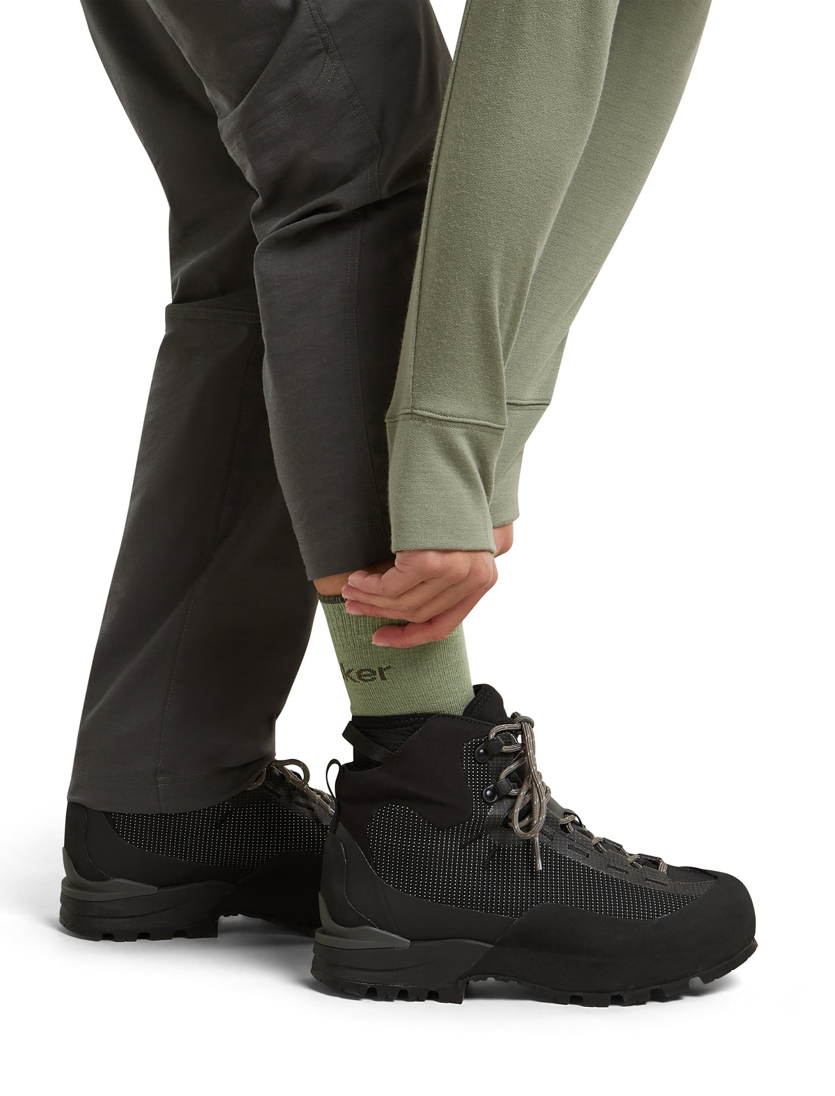 A close-up of a person's lower legs wearing black hiking boots, dark gray pants, and an olive green crew sock with the brand name 'Trek' partially visible. - Icebreaker Merino Hike+ Light Crew Socks (Women's) - Lichen/Dark Loden