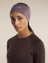 A woman wearing a dusty mauve athletic headband with the brand name 'breaker' printed in white on the forehead, paired with a dark brown long-sleeve top, against a solid beige background. - Icebreaker Merino 200 Oasis Headband (Unisex) - Grey Plum