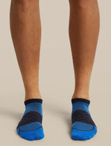 A close-up of a person's feet wearing low-cut athletic socks in blue and dark navy, shown against a plain beige studio background. - Icebreaker Merino Run+ Ultralight Micro Socks (Men's) - Lazurite/Midnight Navy