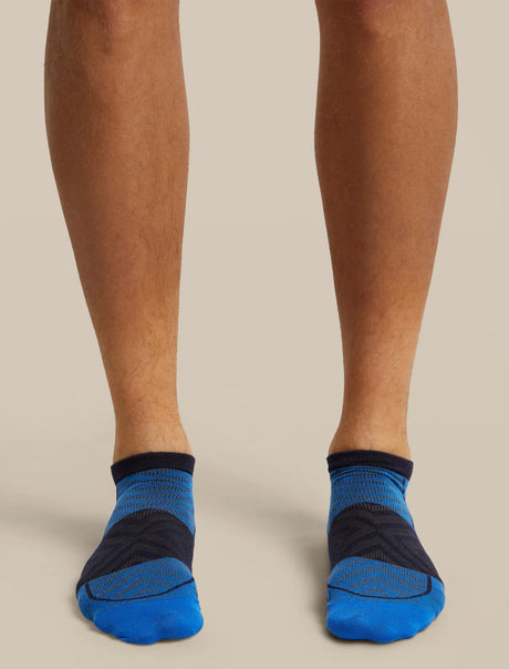 A close-up of a person's feet wearing low-cut athletic socks in blue and dark navy, shown against a plain beige studio background. - Icebreaker Merino Run+ Ultralight Micro Socks (Men's) - Lazurite/Midnight Navy
