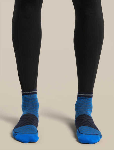 A close-up of a person's legs wearing black leggings and bright blue athletic socks with dark navy heel and toe sections, set against a solid beige background. - Icebreaker Merino Run+ Ultralight Mini Socks (Men's) - Lazurite/Midnight Navy