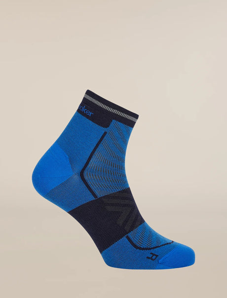 A single athletic ankle sock in blue and dark navy, shown floating against a solid light beige background. The sock features a blue heel and toe, a dark navy compression zone across the instep, and a ribbed navy cuff with the brand name 'Skechers' visible. - Icebreaker Merino Run+ Ultralight Mini Socks (Men's) - Lazurite/Midnight Navy