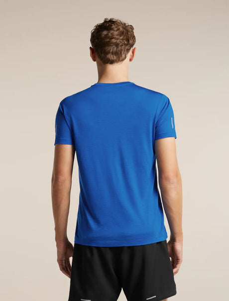 A man viewed from the back wearing a bright blue short-sleeve athletic t-shirt and black shorts against a plain beige studio background. - Icebreaker Merino Blend 125 Cool-Lite Speed Short Sleeve T-Shirt (Men's) - Lazurite