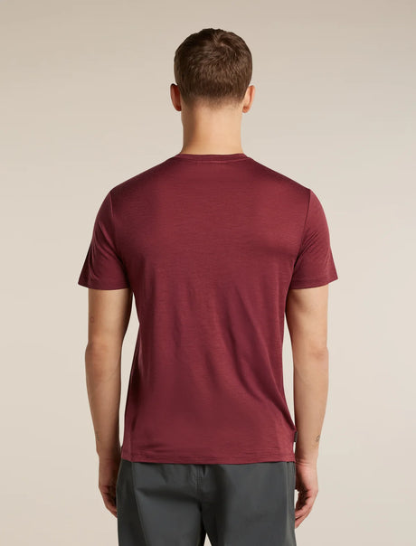 A man viewed from behind wearing a short-sleeve crew-neck t-shirt in a heathered burgundy red, paired with dark gray pants, against a plain beige studio background. - Icebreaker Merino 150 Tech Lite Short Sleeve T-Shirt (Men's) - Port
