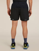 Rear view of a person wearing black athletic shorts, a dark navy top, blue socks, and running shoes against a plain beige studio background. - Icebreaker Merino Blend 125 ZoneKnit Speed 6" Shorts (Men's) - Black