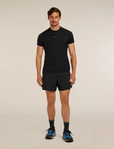 A man modeling a black short-sleeve athletic t-shirt and black running shorts, paired with dark socks and blue running shoes, against a plain beige studio background. - Icebreaker Merino Blend 125 ZoneKnit Speed 6" Shorts (Men's) - Black