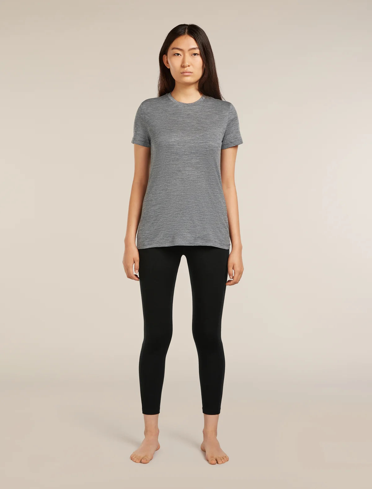 A woman stands barefoot against a plain beige studio background, wearing a heather gray short-sleeve crewneck top and black leggings. - Icebreaker Merino 260 Fastray 25" High Rise Tights (Women's) - Black