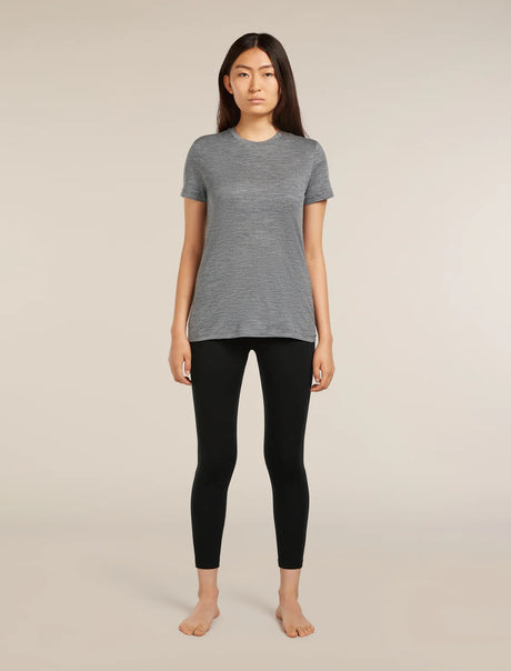 A woman stands barefoot against a plain beige studio background, wearing a heather gray short-sleeve crewneck top and black leggings. - Icebreaker Merino 260 Fastray 25" High Rise Tights (Women's) - Black