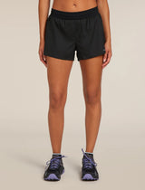 A model from the waist down wearing black athletic shorts and black trail running shoes with purple laces, set against a solid light beige background. - Icebreaker Merino Blend 125 ZoneKnit Speed 3" Shorts (Women's) - Black