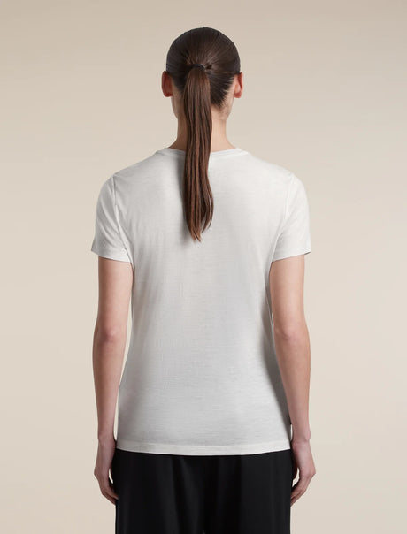 A woman viewed from the back wearing a plain white short-sleeve crew-neck T-shirt and black pants, standing against a light beige studio background. - Icebreaker Merino 150 Tech Lite Short Sleeve T-Shirt (Women's) - Ecru Heather