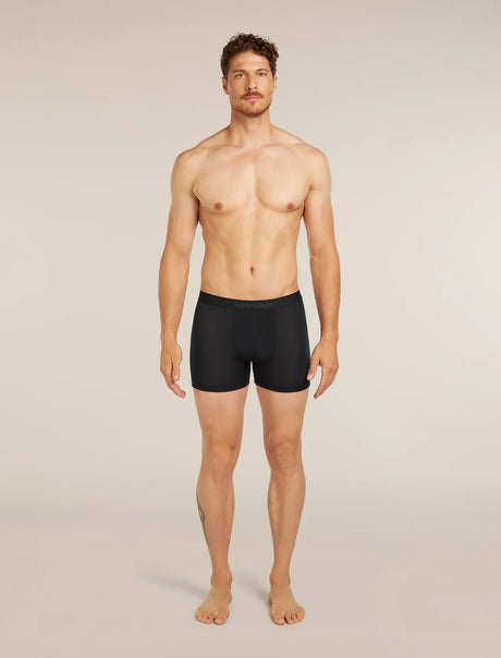 A shirtless male model standing against a plain light beige studio background, wearing black boxer briefs. - Icebreaker Merino Blend 125 Cool-Lite Anatomica Boxers (Men's) - Black