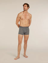 A shirtless male model stands barefoot against a plain light beige studio background, wearing gray heathered boxer briefs. - Icebreaker Merino Blend 125 Cool-Lite Anatomica Boxers (Men's) - Gritstone Heather