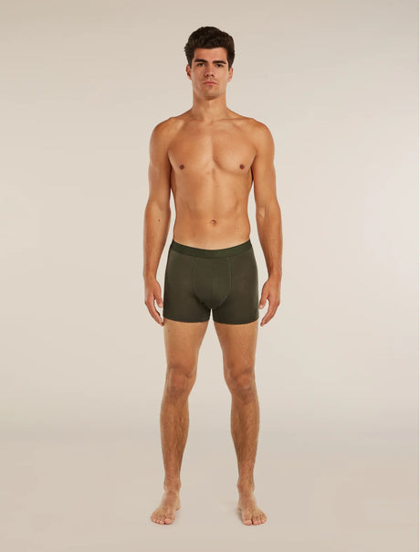 A shirtless male model standing against a plain light beige studio background, wearing dark olive green boxer briefs. - Icebreaker Merino Blend 125 Cool-Lite Anatomica Boxers (Men's) - Dark Loden