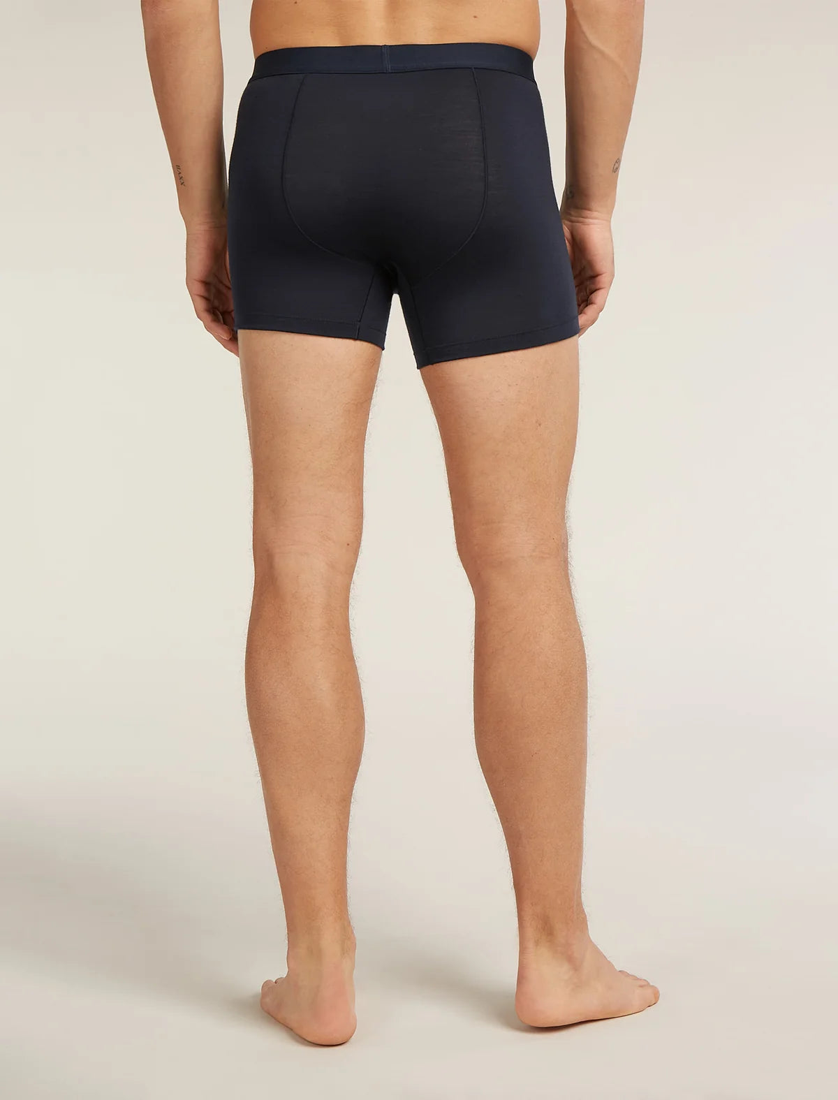 A man viewed from the back wearing dark navy blue boxer briefs, standing barefoot against a plain light beige studio background. - Icebreaker Merino Blend 125 Cool-Lite Anatomica Boxers (Men's) - Midnight Navy