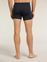 A man viewed from the back wearing dark navy blue boxer briefs, standing barefoot against a plain light beige studio background. - Icebreaker Merino Blend 125 Cool-Lite Anatomica Boxers (Men's) - Midnight Navy