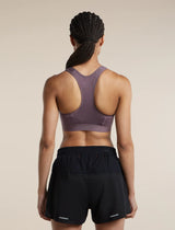 Rear view of a woman wearing a mauve-purple athletic sports bra and black athletic shorts against a plain beige studio background. - Icebreaker Merino Blend 125 ZoneKnit Racerback Bra (Women's) - Grey Plum