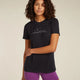 A woman modeling a black short-sleeve t-shirt with a white mountain and moon graphic on the chest, paired with purple athletic shorts, against a solid light beige background. - Icebreaker Merino 150 Tech Lite Short Sleeve T-Shirt Sparkling Stars (Women's) - Black