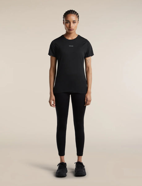 A model stands facing forward wearing a black short-sleeve athletic t-shirt with a small white logo on the chest, black leggings, and black sneakers, set against a solid beige studio background. - Icebreaker Merino Blend 125 Cool-Lite Speed Short Sleeve T-Shirt (Women's) - Black