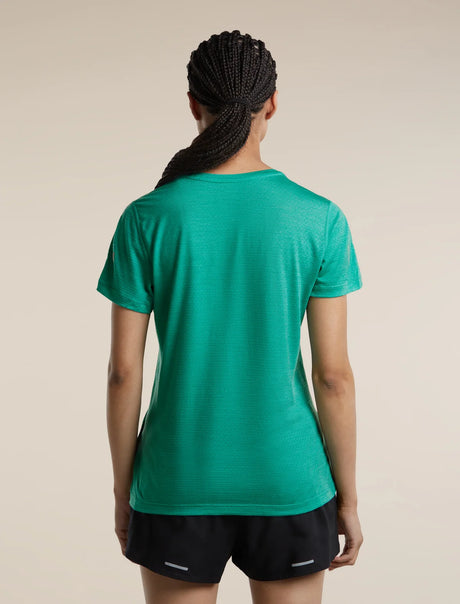 A woman viewed from behind wearing a vibrant green short-sleeve athletic t-shirt and black running shorts against a solid beige background. - Icebreaker Merino Blend 125 Cool-Lite Speed Short Sleeve T-Shirt (Women's) - Fresh