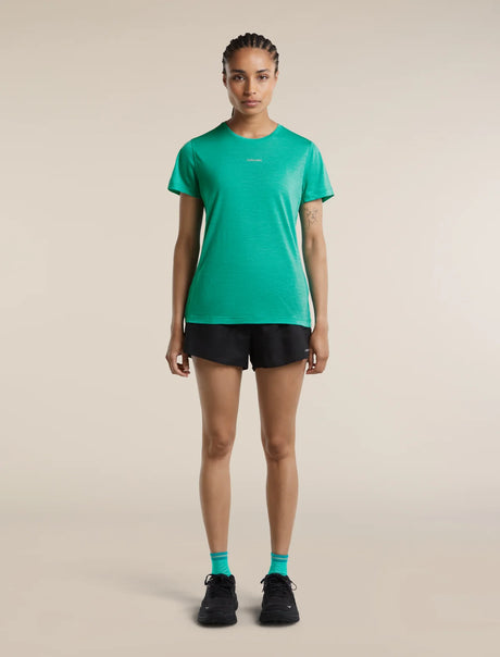 A woman stands facing forward in a studio wearing a bright green athletic short-sleeve T-shirt, black running shorts, black shoes, and bright green socks against a plain warm beige background. - Icebreaker Merino Blend 125 Cool-Lite Speed Short Sleeve T-Shirt (Women's) - Fresh