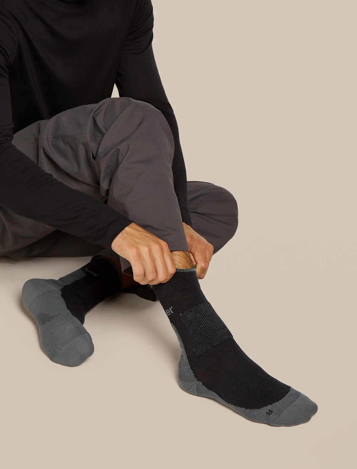 Person wearing black socks with gray soles on a beige background - Icebreaker Merino Hike+ Medium Crew Socks (Men's) - Black/Obsidian