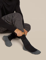 Person wearing black socks with gray soles on a beige background - Icebreaker Merino Hike+ Medium Crew Socks (Men's) - Black/Obsidian
