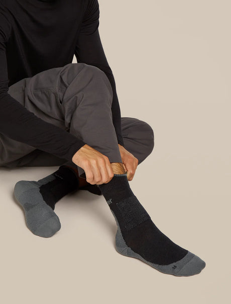Person wearing black socks with gray soles on a beige background - Icebreaker Merino Hike+ Medium Crew Socks (Men's) - Black/Obsidian