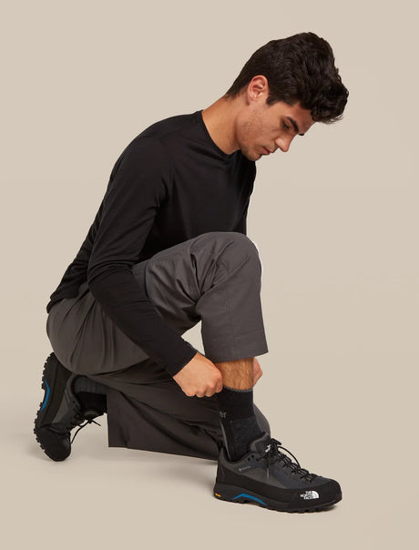 Person wearing black athletic shoes on a beige background - Icebreaker Merino Hike+ Medium Crew Socks (Men's) - Black/Obsidian