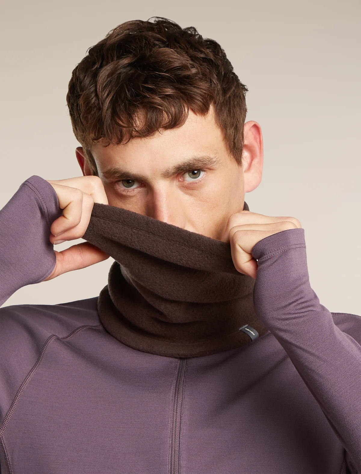 A man wearing a dark brown fleece neck warmer pulled up over his lower face, paired with a purple athletic zip-up jacket, against a plain beige studio background. - Icebreaker Merino Blend 800 RealFleece Classic Pile Chute (Unisex) - Bittersweet
