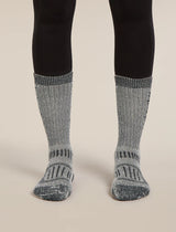 Gray socks with black patterns worn with black leggings on a beige background - Icebreaker Merino Hike+ Mountaineer Mid Calf Socks (Women's) - Jet Heather/Black