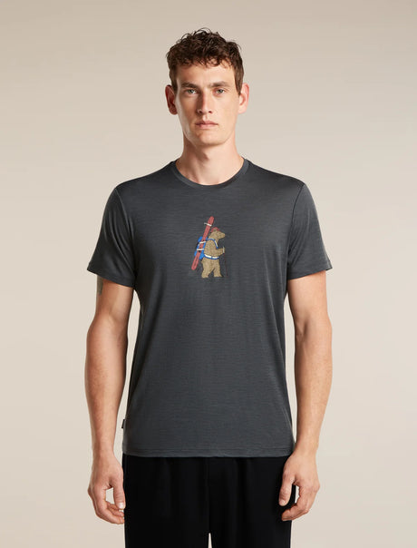 A man wearing a dark gray heathered t-shirt with a small graphic of a bear carrying a ski pole on the chest, standing against a solid beige background. - Icebreaker Merino 150 Tech Lite Short Sleeve T-Shirt Bear Tour (Men's) - Obsidian