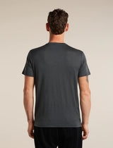 A man viewed from behind wearing a dark charcoal gray short-sleeve athletic t-shirt and black pants, standing against a solid light beige background. - Icebreaker Merino 150 Tech Lite Short Sleeve T-Shirt Bear Tour (Men's) - Obsidian