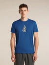 A man wearing a royal blue crewneck t-shirt with a distressed white graphic of a bear carrying a ski pole, paired with dark gray athletic pants, against a solid beige studio background. - Icebreaker Merino 150 Tech Lite Short Sleeve T-Shirt Bear Tour (Men's) - Lazurite