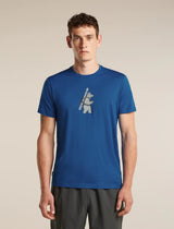 A man wearing a royal blue crewneck t-shirt with a distressed white graphic of a bear carrying a ski pole, paired with dark gray athletic pants, against a solid beige studio background. - Icebreaker Merino 150 Tech Lite Short Sleeve T-Shirt Bear Tour (Men's) - Lazurite