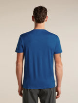 A man viewed from behind wearing a solid blue short-sleeve crewneck t-shirt and dark gray athletic shorts, standing against a plain beige studio background. - Icebreaker Merino 150 Tech Lite Short Sleeve T-Shirt Bear Tour (Men's) - Lazurite