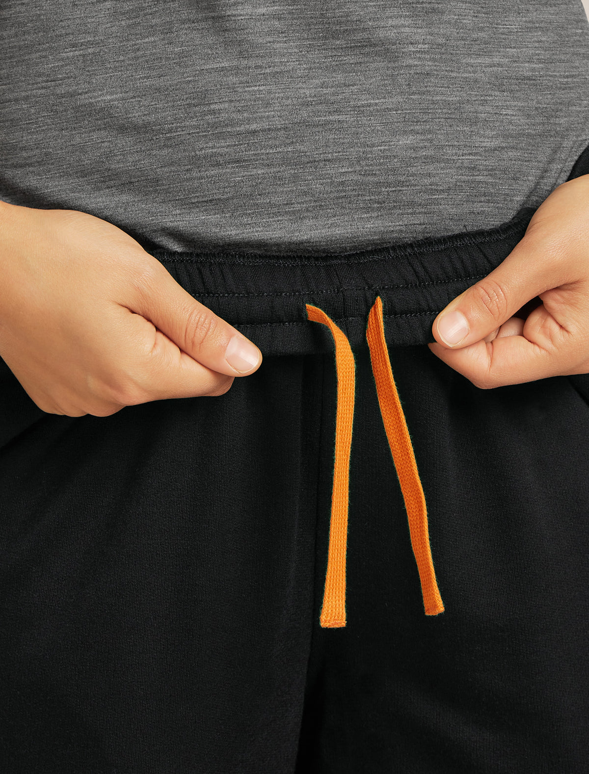 Person adjusting black shorts with orange drawstrings against a gray background - Icebreaker Merino Blend 150 Drift Pants (Women's) - Black
