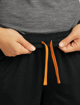 Person adjusting black shorts with orange drawstrings against a gray background - Icebreaker Merino Blend 150 Drift Pants (Women's) - Black