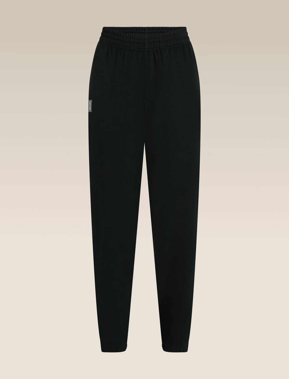Black jogger-style pants with an elastic waistband and a small white embroidered logo on the left hip, shown against a light beige gradient background. - Icebreaker Merino Blend 150 Drift Pants (Women's) - Black