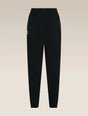 Black jogger-style pants with an elastic waistband and a small white embroidered logo on the left hip, shown against a light beige gradient background. - Icebreaker Merino Blend 150 Drift Pants (Women's) - Black