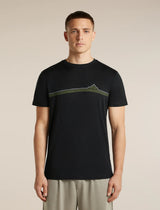 A man wearing a black short-sleeve crewneck t-shirt with a green and yellow mountain graphic across the chest, paired with light gray trousers, set against a plain beige studio background. - Icebreaker Merino 150 Tech Lite Short Sleeve T-Shirt Range Stripes (Men's) - Black