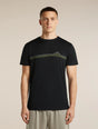 A man wearing a black short-sleeve crewneck t-shirt with a green and yellow mountain graphic across the chest, paired with light gray trousers, set against a plain beige studio background. - Icebreaker Merino 150 Tech Lite Short Sleeve T-Shirt Range Stripes (Men's) - Black
