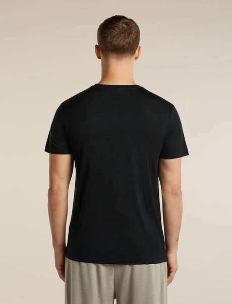 A man viewed from the back wearing a plain black short-sleeve crew-neck t-shirt and light beige trousers, standing against a solid light beige background. - Icebreaker Merino 150 Tech Lite Short Sleeve T-Shirt Range Stripes (Men's) - Black
