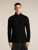 A man wearing a black long-sleeve quarter-zip athletic pullover with a textured waffle knit pattern, standing against a solid light beige background. - Icebreaker Merino 400 RealFleece Grid Peaksland Long Sleeve Half Zip (Men's) - Black