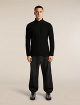 A man modeling a black long-sleeve quarter-zip athletic top with black jogger pants and black sneakers, standing against a solid light beige studio background. - Icebreaker Merino 400 RealFleece Grid Peaksland Long Sleeve Half Zip (Men's) - Black