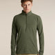 A man wearing an olive green quarter-zip long-sleeve waffle knit pullover sweater and khaki pants, standing against a solid beige studio background. - Icebreaker Merino 400 RealFleece Grid Peaksland Long Sleeve Half Zip (Men's) - Dark Loden