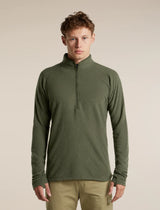 A man wearing an olive green quarter-zip long-sleeve waffle knit pullover sweater and khaki pants, standing against a solid beige studio background. - Icebreaker Merino 400 RealFleece Grid Peaksland Long Sleeve Half Zip (Men's) - Dark Loden