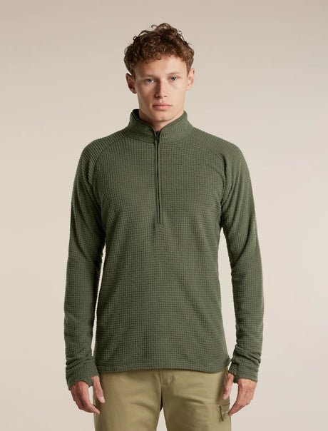 A man wearing an olive green quarter-zip long-sleeve waffle knit pullover sweater and khaki pants, standing against a solid beige studio background. - Icebreaker Merino 400 RealFleece Grid Peaksland Long Sleeve Half Zip (Men's) - Dark Loden